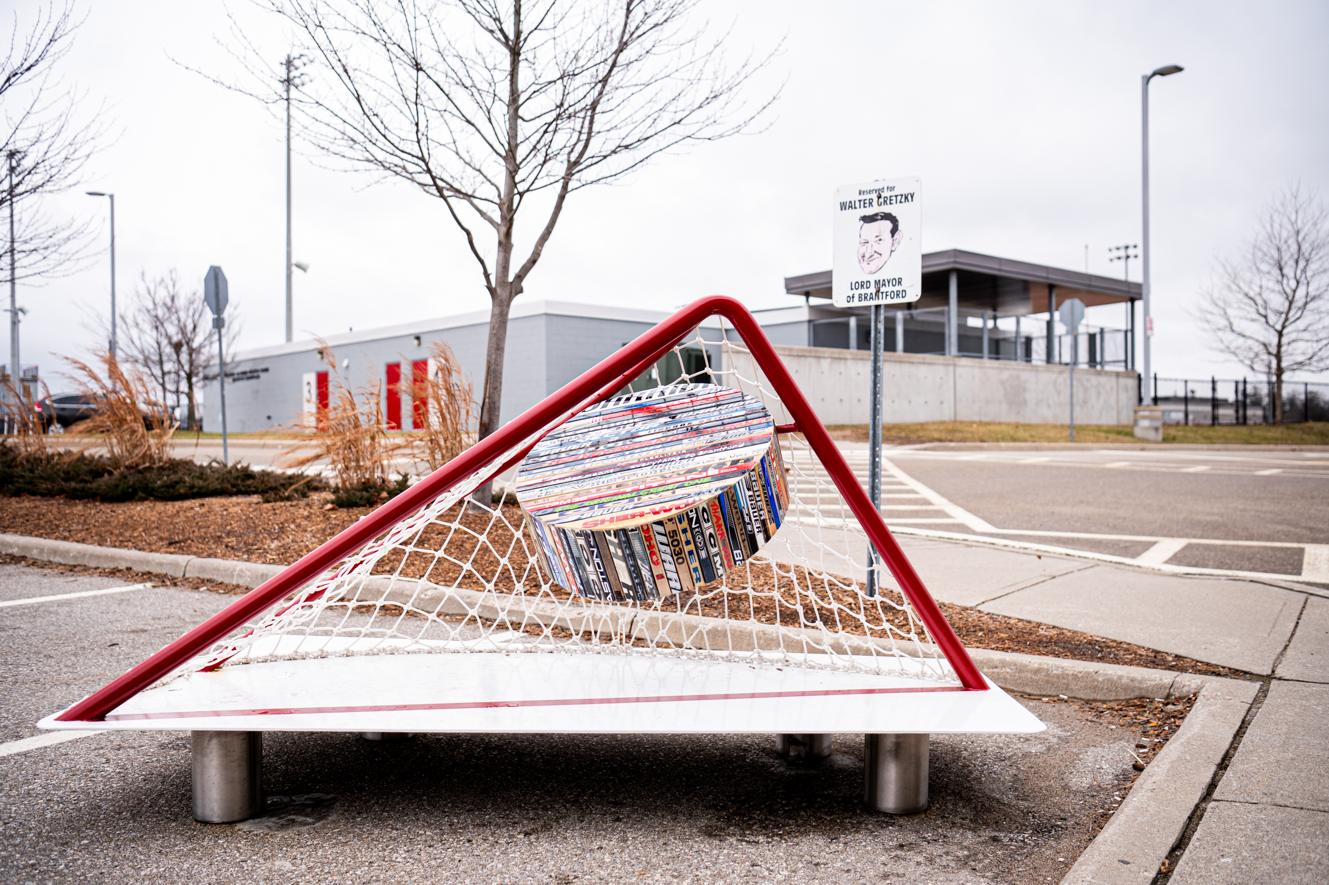 An art piece made of a hockey net with an oversized puck hanging in it. The puck is made of many different pieces of different hockey sticks.