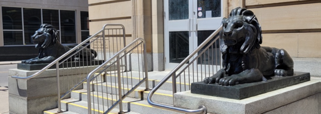 two lion statues flanking a concrete staircase. there are about six steps, ending at a set of glass doors
